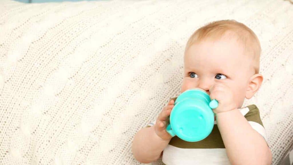 Baby drinks in green sippy cup. 